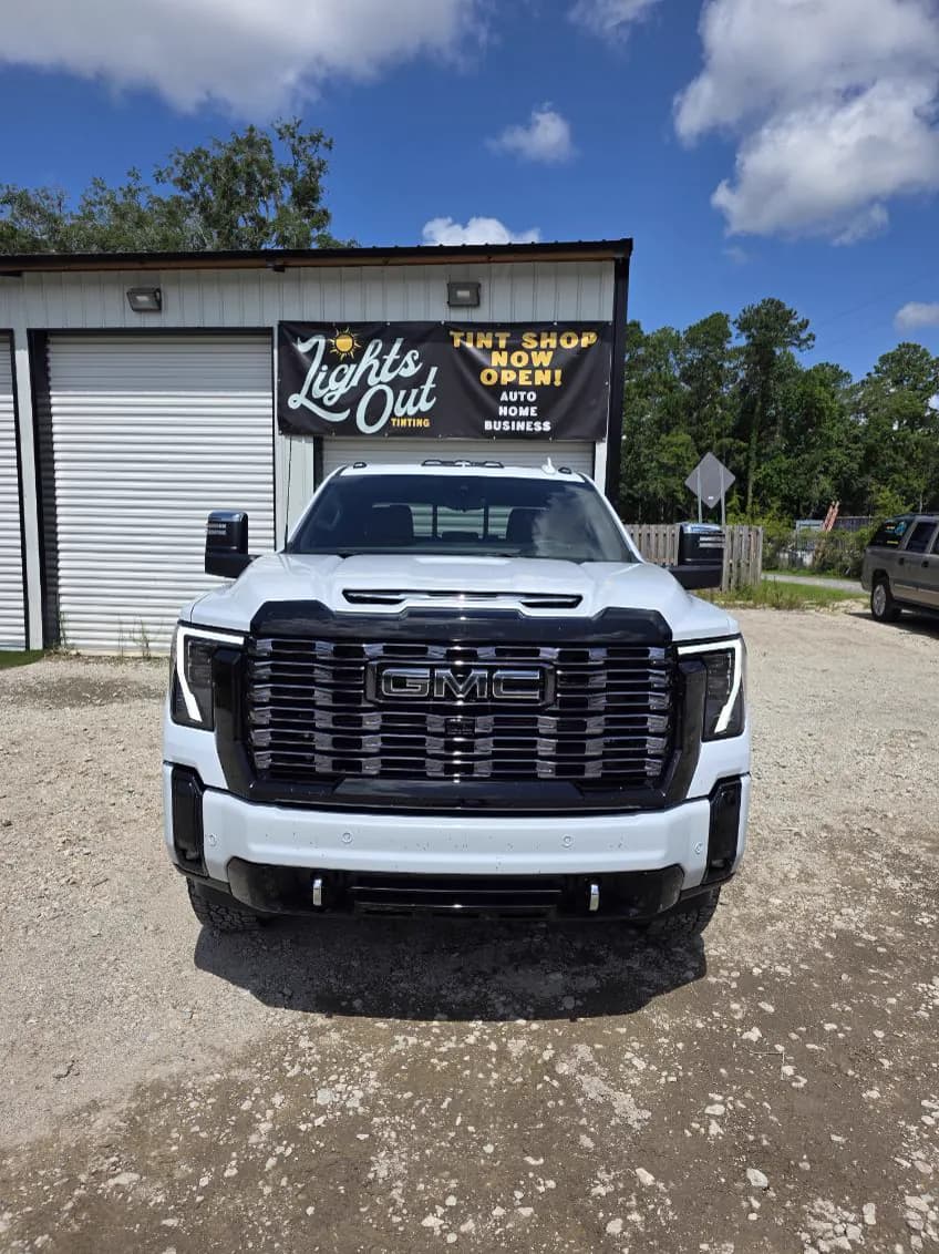 A white GMC Sierra Denali with tinted windows outside the Lights Out Tinting shop.