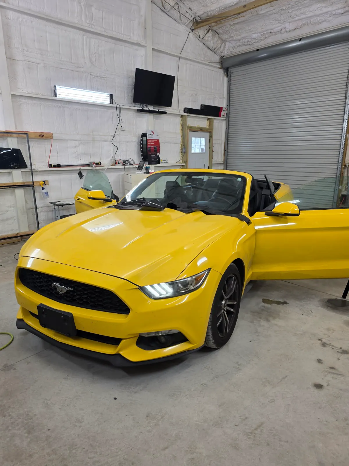 A yellow Mustang convertible with the top down and freshly tinted glass in the shop bay.