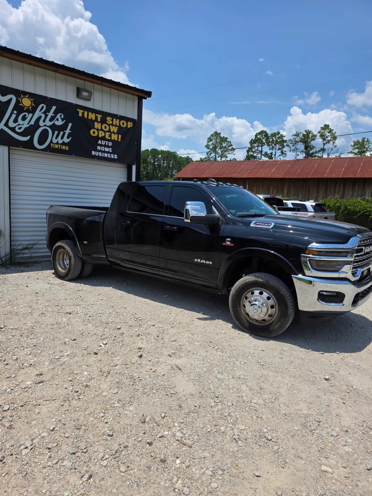 A black Ram dually with freshly tinted windows in front of the hand-painted Lights Out Tinting sign